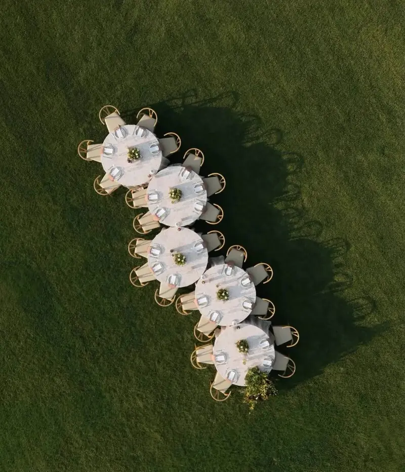 Overhead view of five round tables with white cloths and wood chairs in a row on a green lawn Overhead view of five round tables with white cloths and wood chairs in a row on a green lawn
