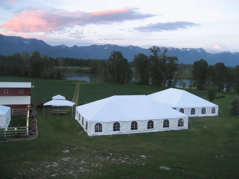 Aerial view of a white tent on a lawn near a red barn, trees and mountains at sunset Aerial view of a white tent on a lawn near a red barn, trees and mountains at sunset