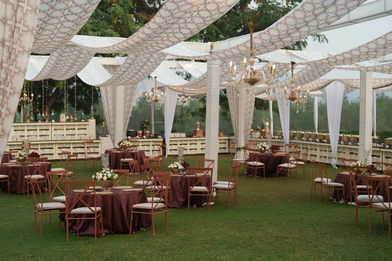 Round tables in burgundy cloths under a canopy with white fabric swags and chandeliers Round tables in burgundy cloths under a canopy with white fabric swags and chandeliers