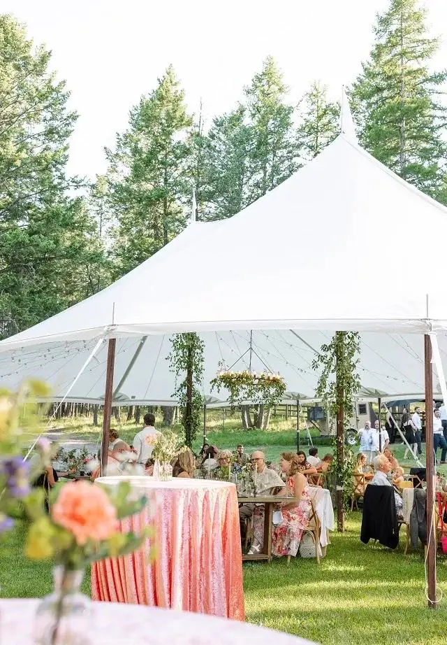Cocktail table in a coral cloth in front of a peaked white tent on a lawn lined with pine trees Cocktail table in a coral cloth in front of a peaked white tent on a lawn lined with pine trees