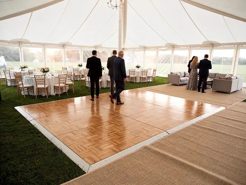 Wood dance floor, round tables, a gray lounge set and a chandelier inside a white frame tent Wood dance floor, round tables, a gray lounge set and a chandelier inside a white frame tent