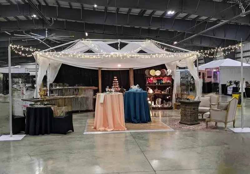 White draped canopy with fairy lights over a lounge and linen display in an indoor exhibit hall White draped canopy with fairy lights over a lounge and linen display in an indoor exhibit hall