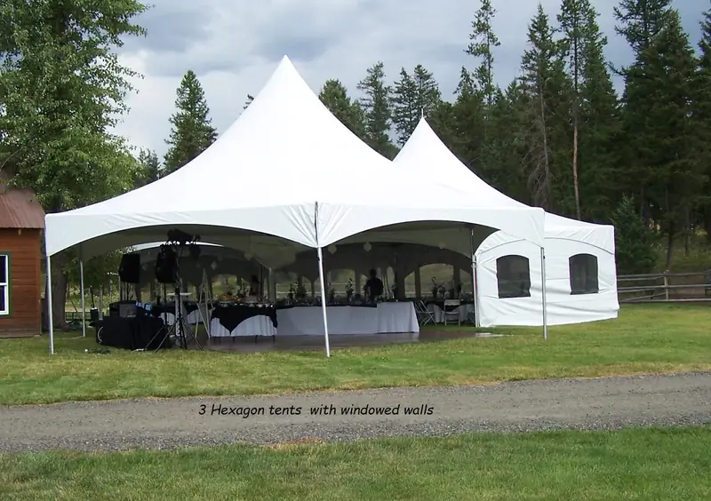 Three white hexagon tents with windowed side walls on a lawn beside a gravel drive