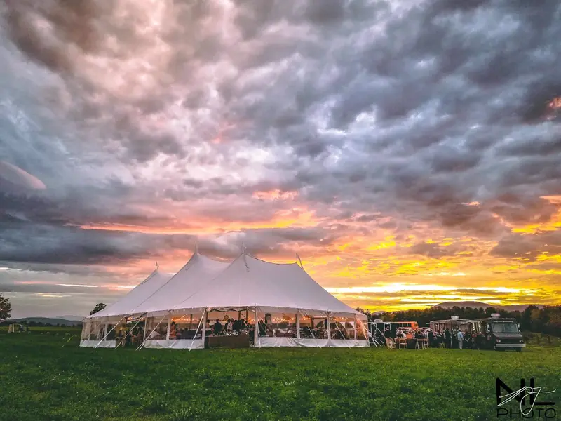 Lit white tent with open sides in a grass field at dusk with mountains in the distance