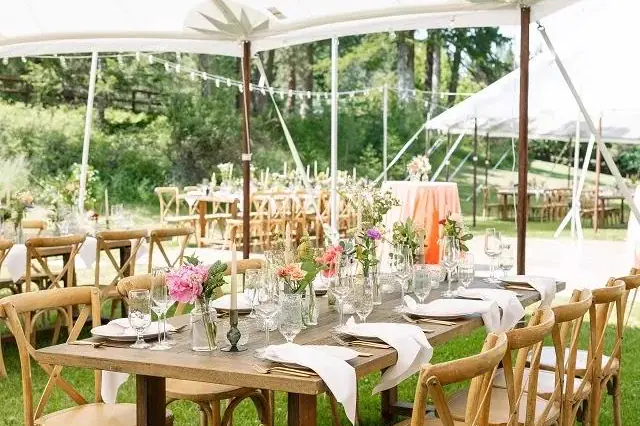 Long wood table with cross-back chairs and coral flowers under a white tent