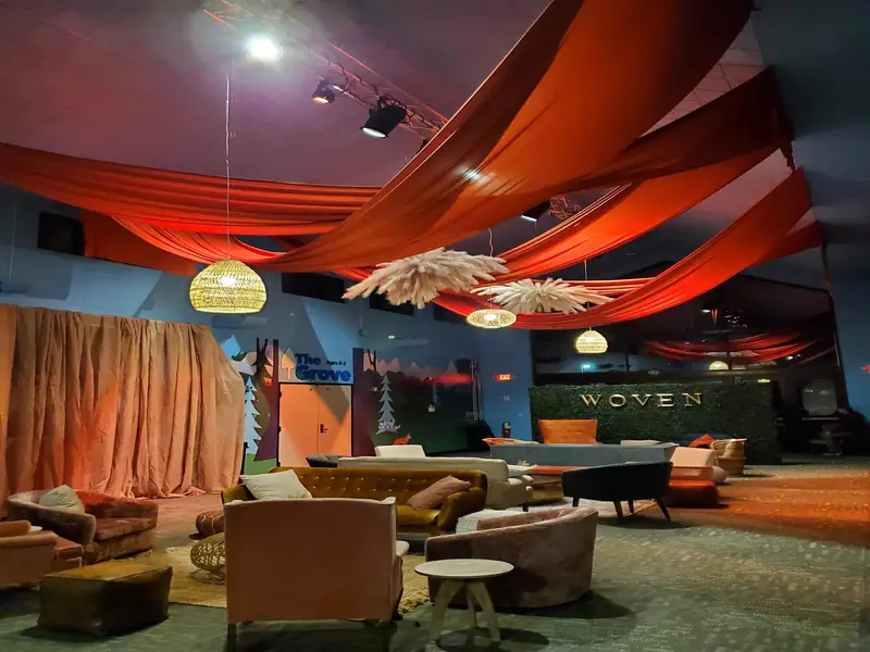 Lounge chairs, sofas and side tables under rust colored ceiling draping and woven pendant lights Lounge chairs, sofas and side tables under rust colored ceiling draping and woven pendant lights