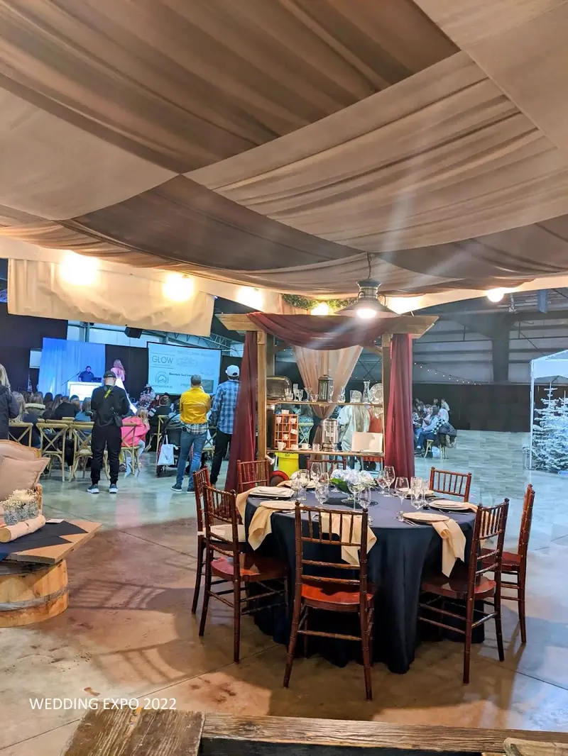 Round table with a navy cloth, wood chairs and a floral centerpiece set up at an indoor wedding expo booth Round table with a navy cloth, wood chairs and a floral centerpiece set up at an indoor wedding expo booth
