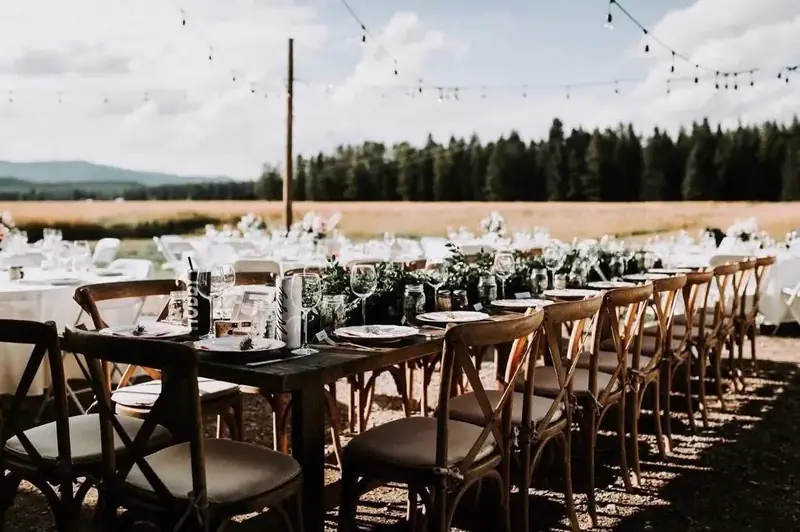 Long dark wood tables with cross-back chairs, greenery runners and string lights outdoors