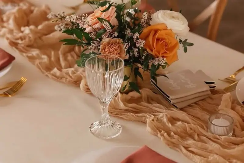 Table setting with a peach runner, orange roses, a crystal goblet and gold flatware Table setting with a peach runner, orange roses, a crystal goblet and gold flatware