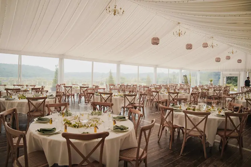 Round tables with cross-back chairs on a wood floor under a draped ceiling with glass walls Round tables with cross-back chairs on a wood floor under a draped ceiling with glass walls