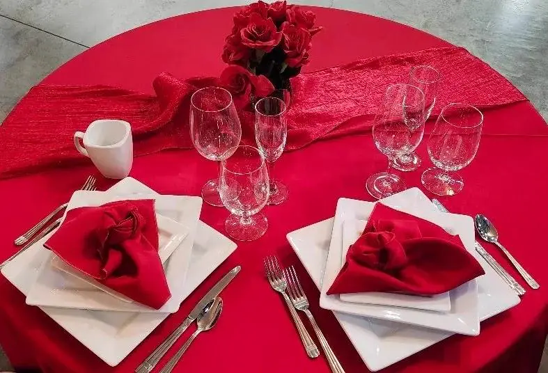 Overhead view of a round table in a red cloth with white plates, red napkins and a vase of red roses Overhead view of a round table in a red cloth with white plates, red napkins and a vase of red roses