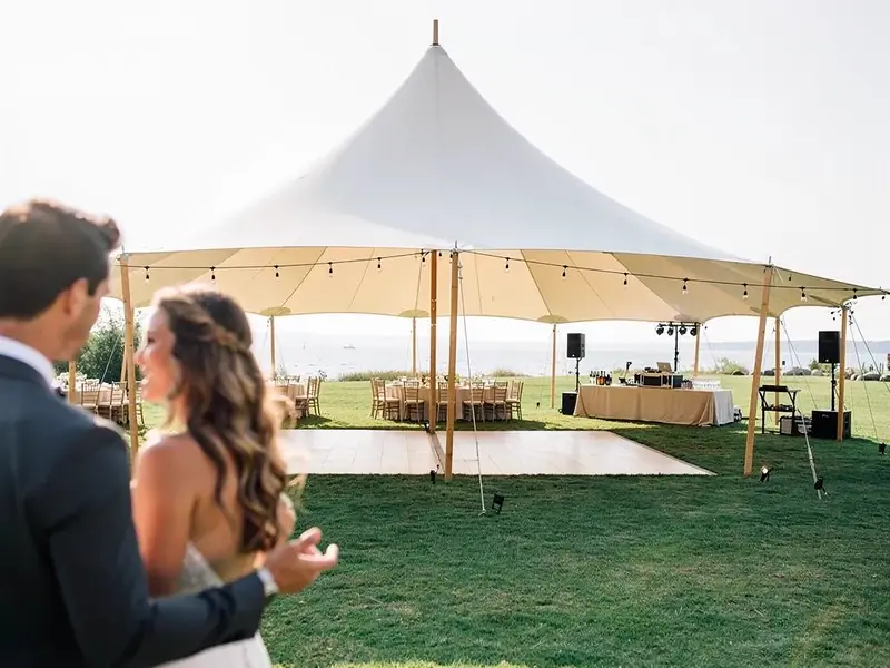 Sailcloth tent with a dance floor, long tables and speakers on a lawn beside a lake Sailcloth tent with a dance floor, long tables and speakers on a lawn beside a lake