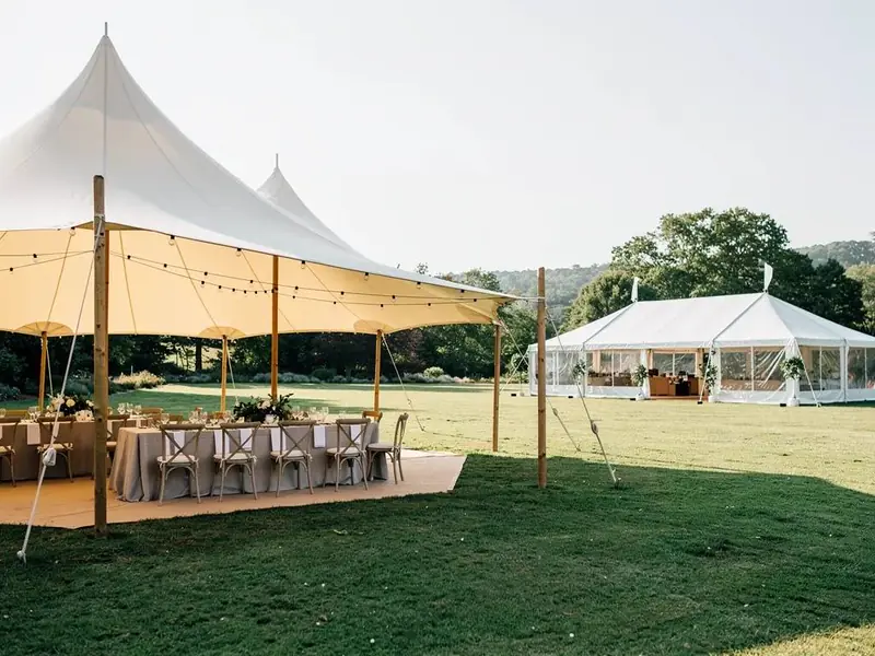 Sailcloth tent over a wood deck with tables and string lights beside a white frame tent Sailcloth tent over a wood deck with tables and string lights beside a white frame tent