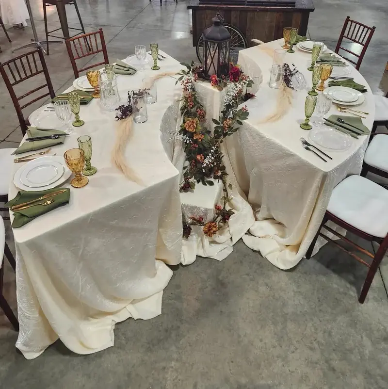 Overhead view of a curved serpentine table with an ivory cloth, greenery runner and dark wood chairs Overhead view of a curved serpentine table with an ivory cloth, greenery runner and dark wood chairs