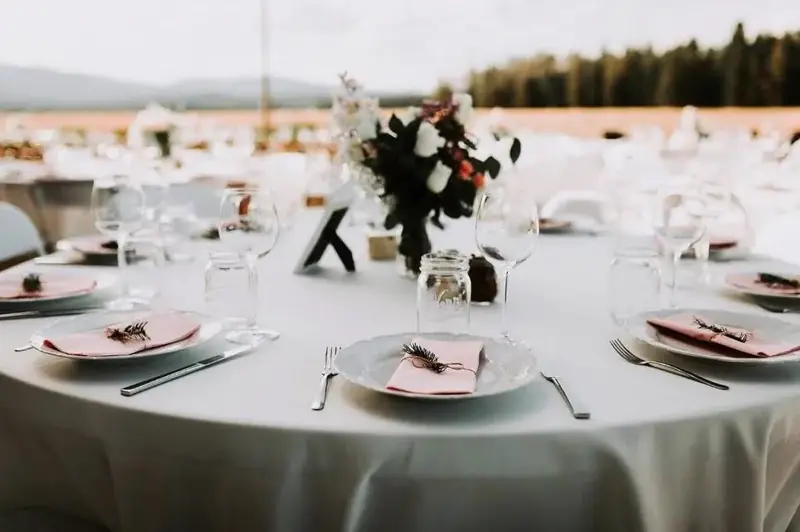 Round table with a pale gray cloth, pink napkins, burgundy flowers and a table number 7 in an open field Round table with a pale gray cloth, pink napkins, burgundy flowers and a table number 7 in an open field