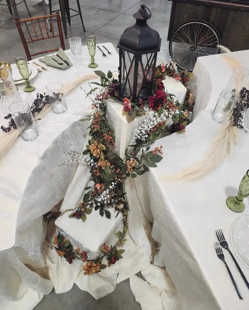 Overhead view of a tiered table display with white cloths, a black lantern and a greenery and berry garland Overhead view of a tiered table display with white cloths, a black lantern and a greenery and berry garland
