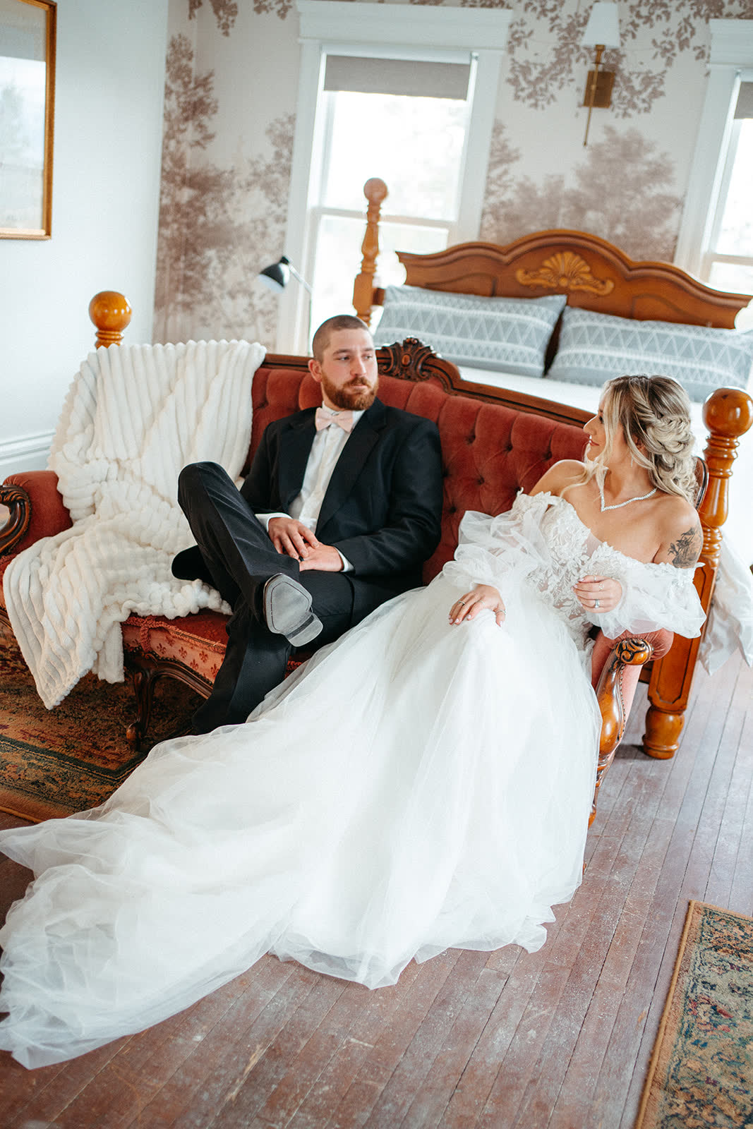Bride and groom resting on a velvet sofa in a farmhouse suite before the ceremony