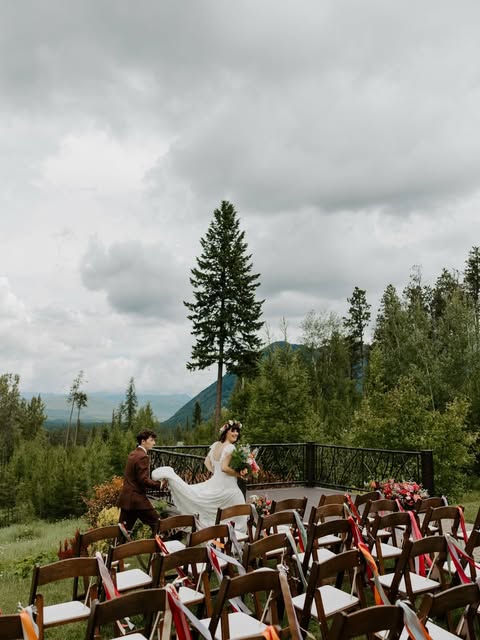 Bride and groom coming up the aisle on a forest deck, guests seated in wooden chairs under tall pines