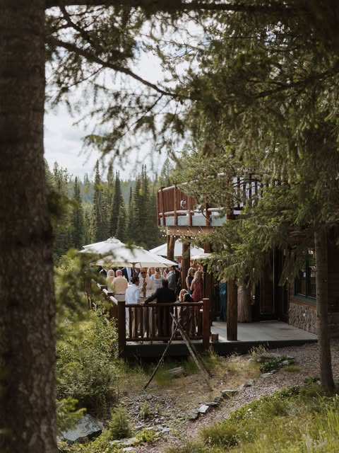 Guests gathered on a deck under market umbrellas and tall pines at a mountain venue