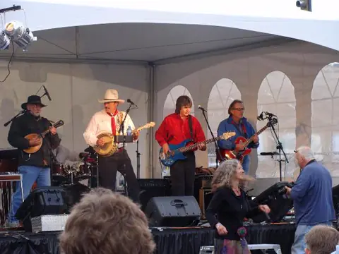 A band plays on a stage under a white tent while people dance in front