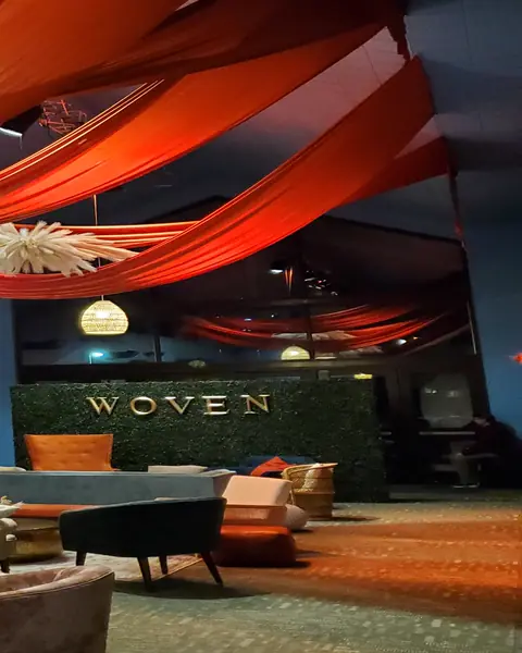 A conference lounge with velvet armchairs, a grey sofa and a green hedge wall under orange ceiling drapes