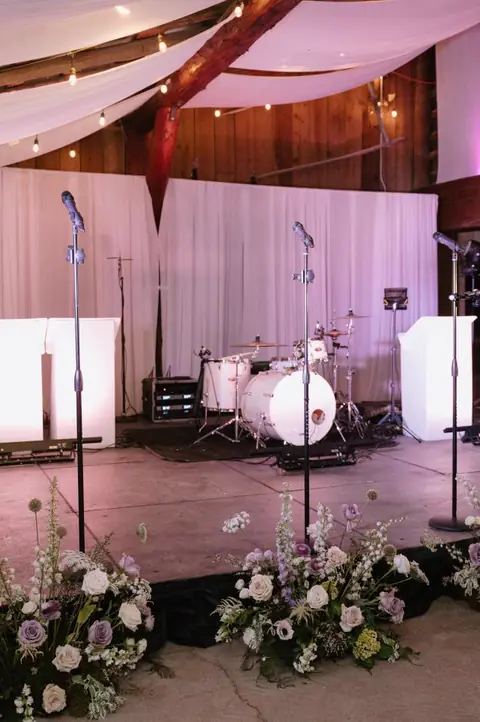 A drum kit and microphones set on a stage trimmed with white flowers