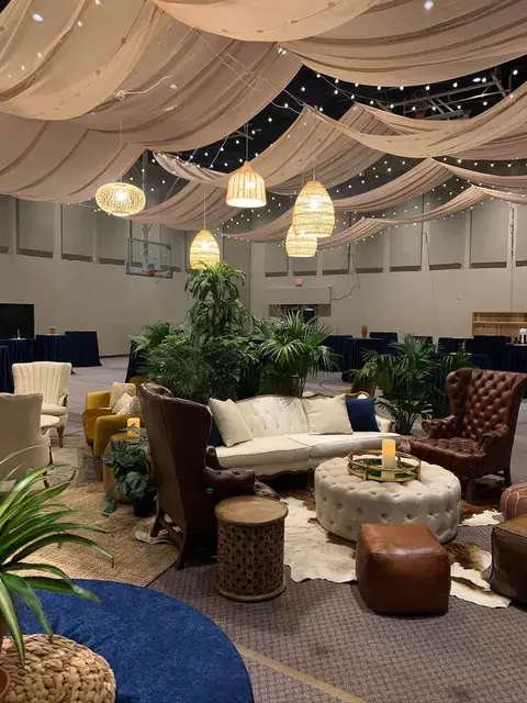 An indoor event lounge with sofas, armchairs and ottomans under hanging wicker pendant lights