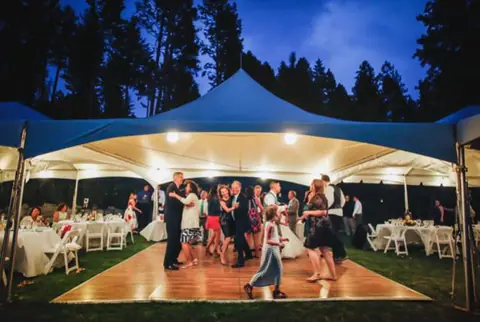 Guests dance under a lit white tent at an evening party