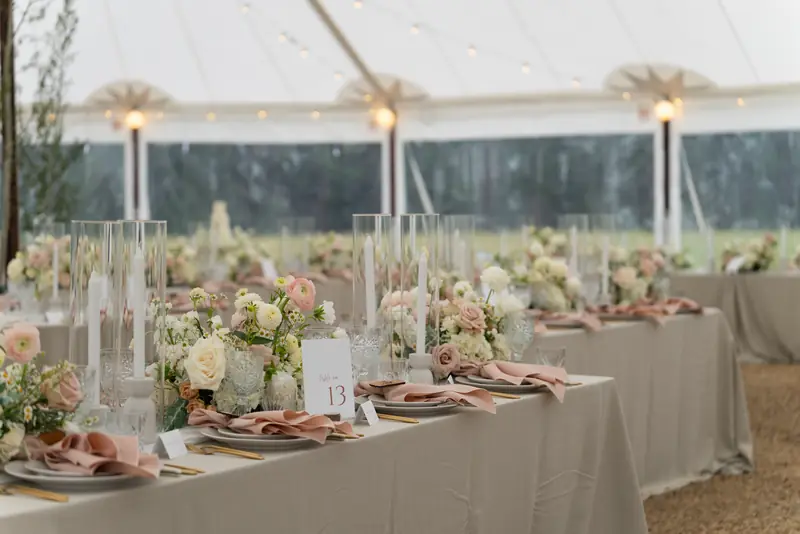 Long decorated dining tables with floral arrangements and candle cylinders filling a tented venue