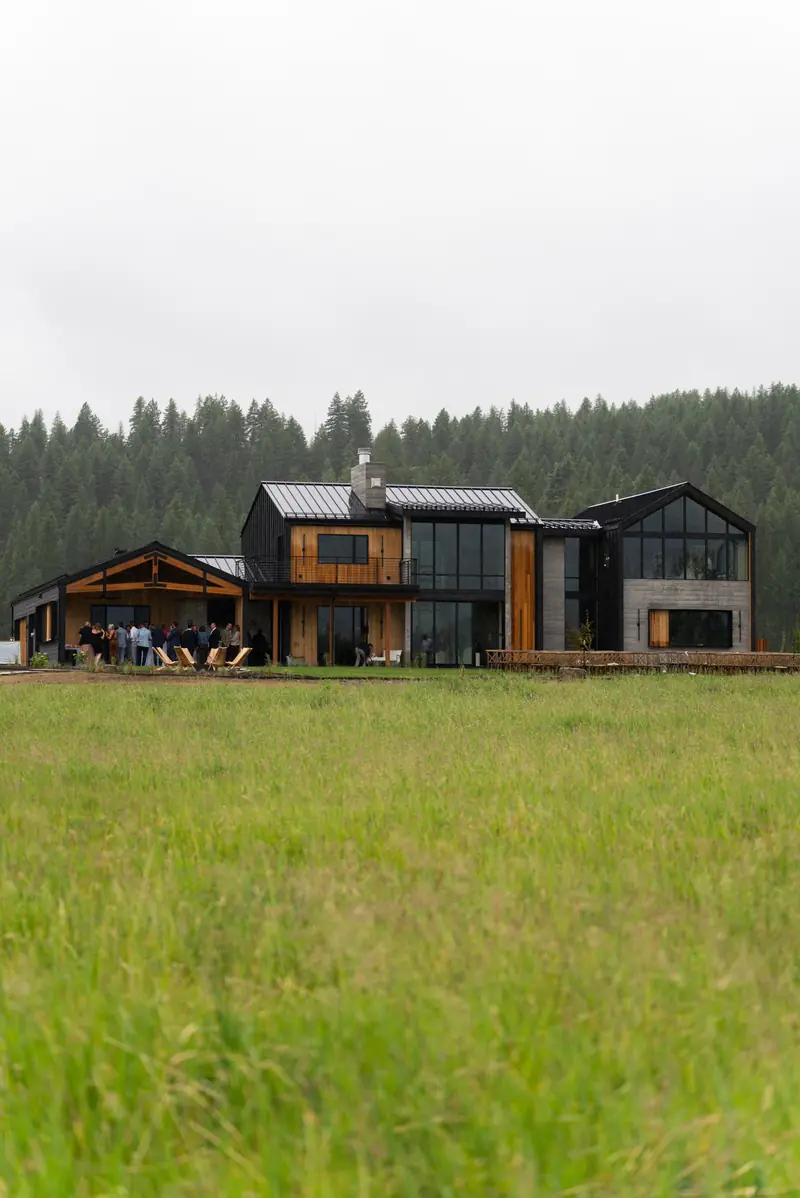 A modern black wood lodge standing in a grassy meadow under an overcast sky
