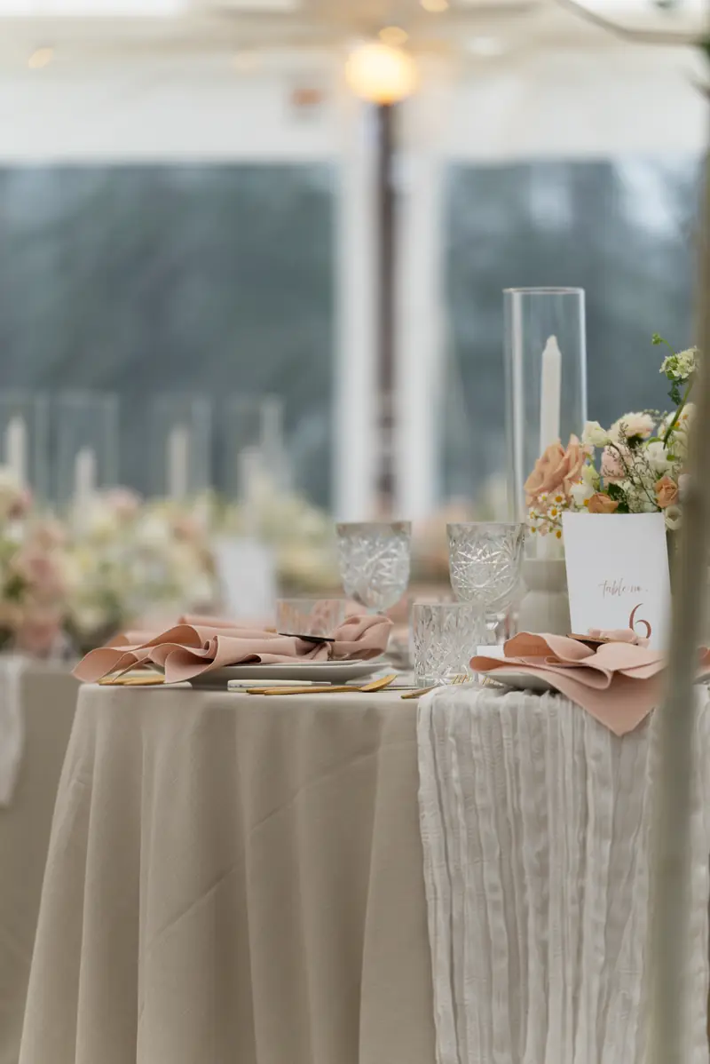 Place settings with candle holders and flowers on a dressed table inside an event tent
