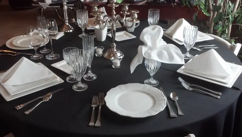 A round table in a black tablecloth set with white plates, folded napkins, crystal stemware and a candelabra A round table in a black tablecloth set with white plates, folded napkins, crystal stemware and a candelabra