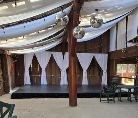 A low stage under white ceiling drapes with disco balls hanging above an event floor A low stage under white ceiling drapes with disco balls hanging above an event floor