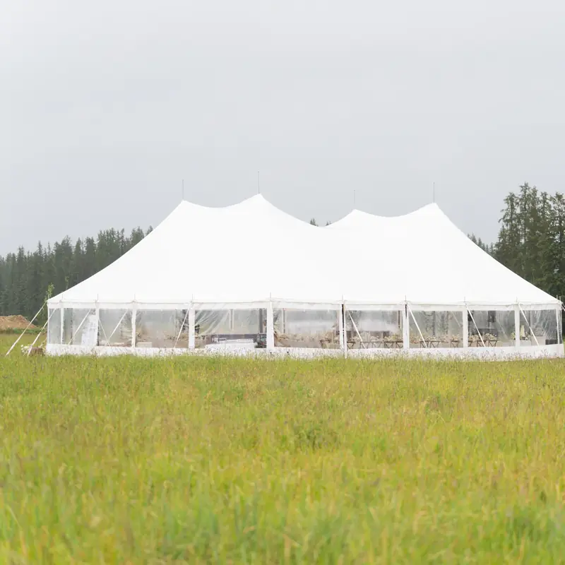 A large white party tent centered in a green meadow with trees behind it