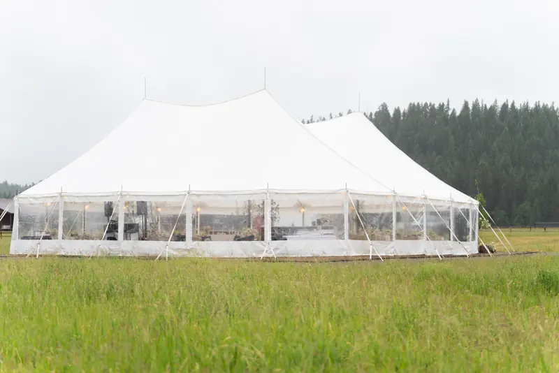 Side view of a white sailcloth tent with a peaked roof in a grassy meadow