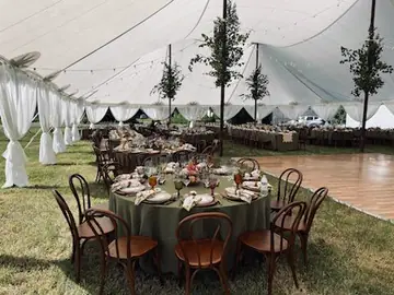 A wood dance floor under a white tent beside round tables with green linens