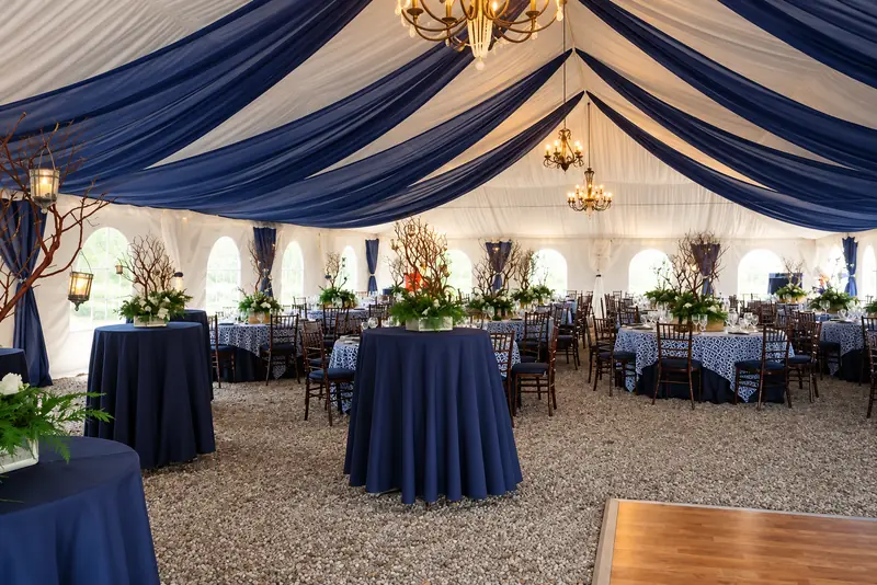 A wood plank dance floor in a tent with navy and white ceiling drapes and three hanging chandeliers A wood plank dance floor in a tent with navy and white ceiling drapes and three hanging chandeliers